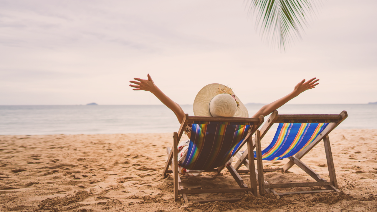 Midlife woman sitting on a Bermuda beach with arms wide open, embracing body love, self-worth, and freedom during a beach vacation.