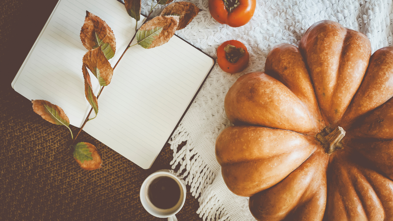 Flat lay of a cozy autumn scene with a pumpkin, an open journal, and a cup of coffee — symbolizing reflection, seasonal transitions, and navigating life transitions.