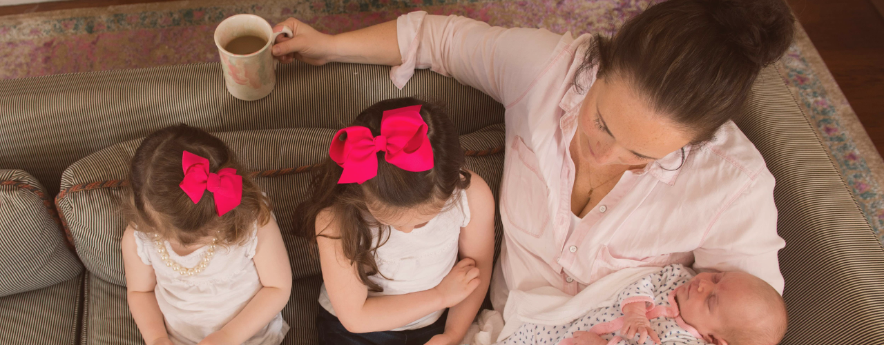 Postpartum mom recovering from burnout and people pleasing, reading with her kids on the couch while holding coffee