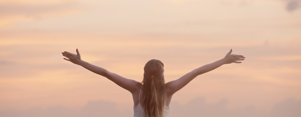 Midlife woman facing the ocean with arms outstretched, symbolizing freedom, transformation, and spiritual awakening during a midlife crisis in women