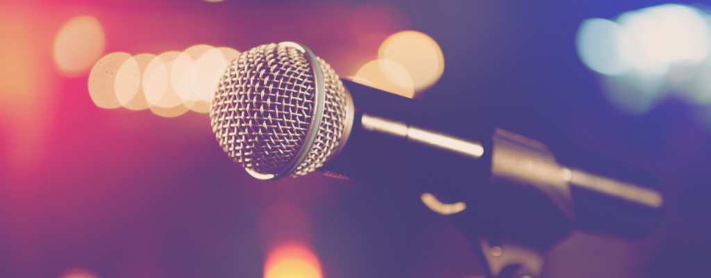 Close-up of a microphone in focus with a blurred background, representing public speaking, women’s empowerment, leadership panels, and sharing personal stories in front of an audience.