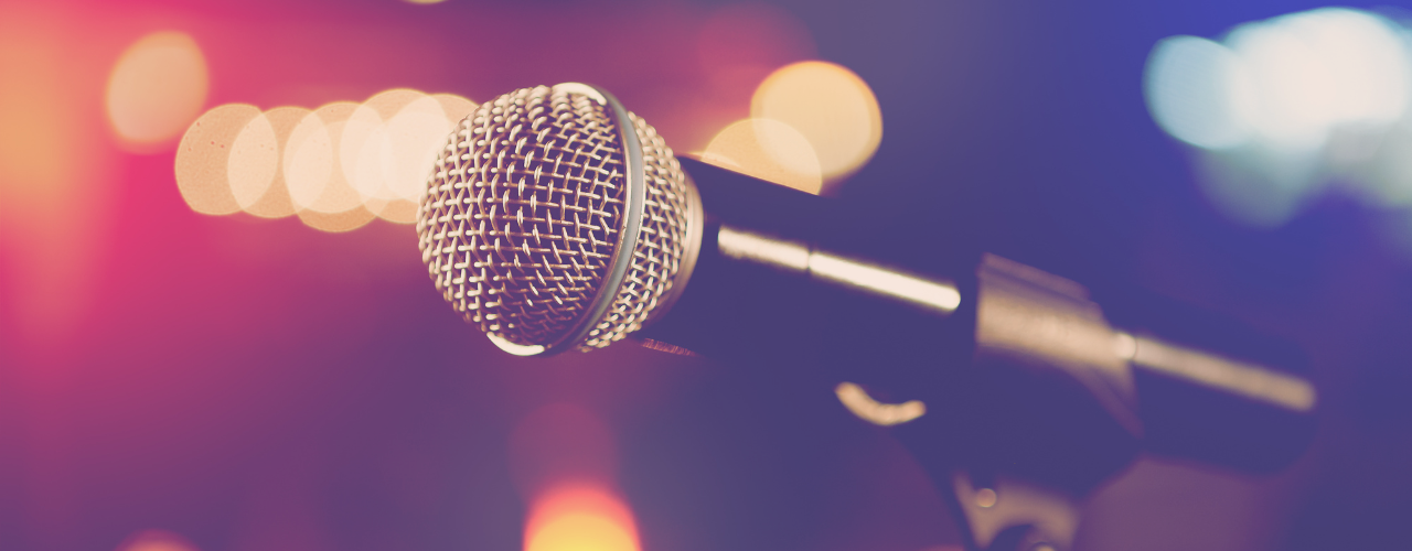 Close-up of a microphone in focus with a blurred background, representing public speaking, women’s empowerment, leadership panels, and sharing personal stories in front of an audience.